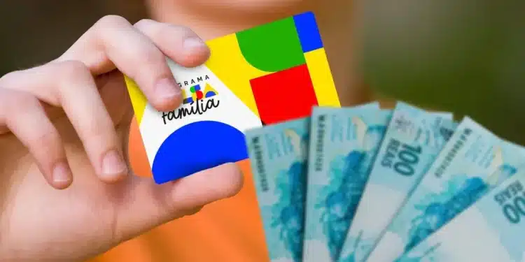 Mão segurando cartão do Bolsa Família com notas de reais ao fundo, ilustrando o pagamento do benefício conforme o NIS nesta quarta-feira (24).