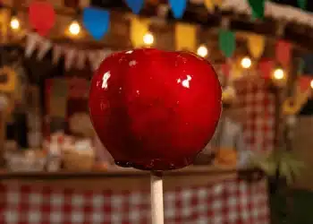 Maçã do amor brilhante em destaque em barraca de festa junina, representando o plural correto do doce típico