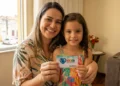 Mãe sorrindo com filha segurando cartão do Programa Mães de Pernambuco.