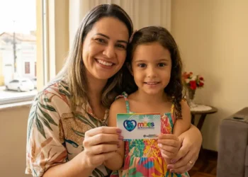 Mãe sorrindo com filha segurando cartão do Programa Mães de Pernambuco.