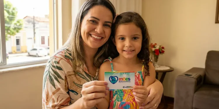 Mãe sorrindo com filha segurando cartão do Programa Mães de Pernambuco.