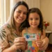 Mãe sorrindo com filha segurando cartão do Programa Mães de Pernambuco.