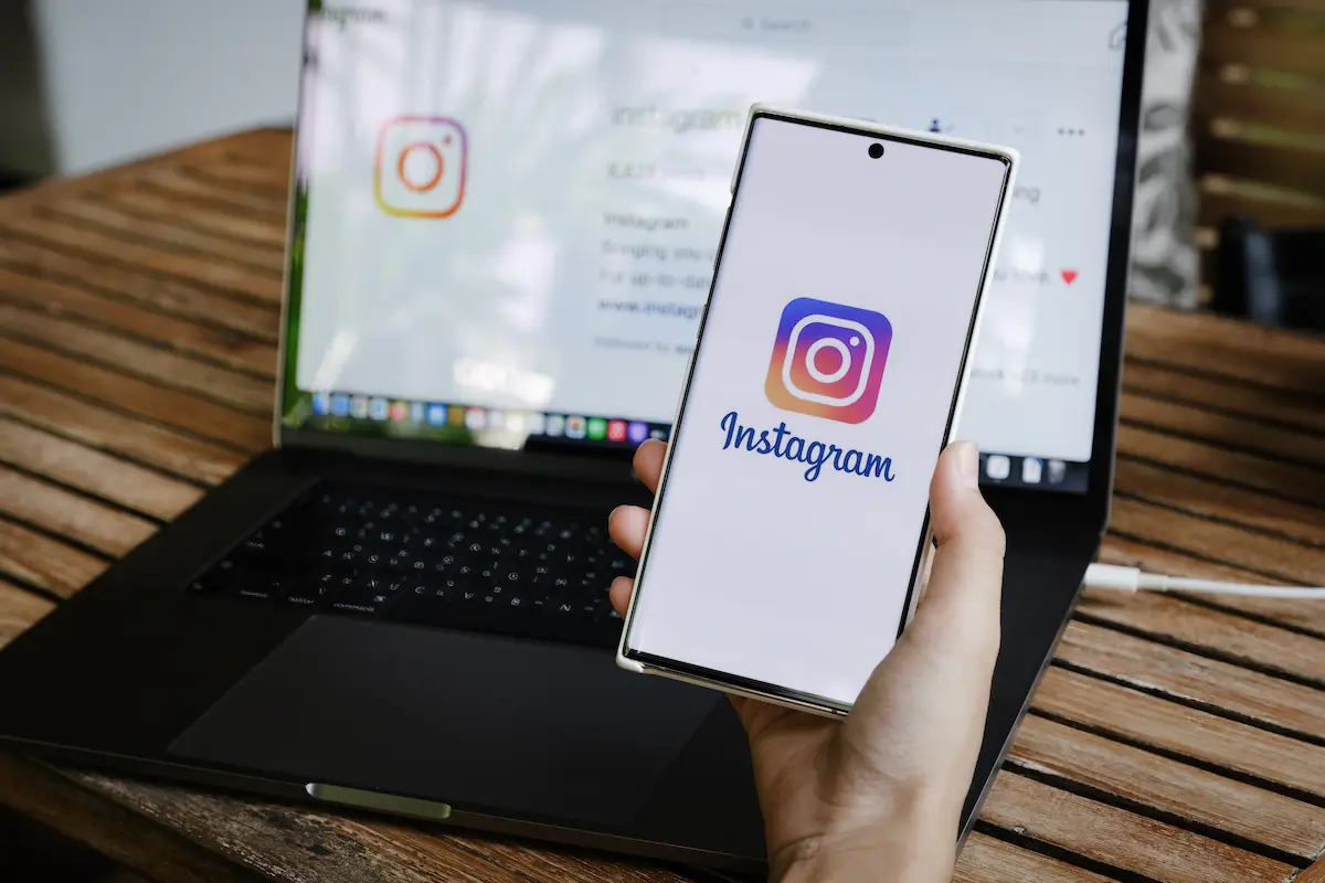Pessoa segura celular com a tela inicial do Instagram aberta, com notebook ao fundo, em contexto de discussão sobre privacidade digital e compliance nas redes sociais.