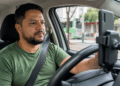 Motorista de aplicativo brasileiro dentro do carro utilizando smartphone no painel durante o trabalho.