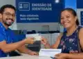 Atendente entregando nova Carteira de Identidade à cidadã, representando o mutirão de emissão de documento nos dias 26 e 27 de junho