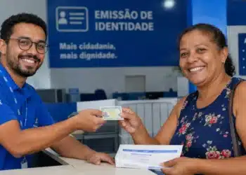 Atendente entregando nova Carteira de Identidade à cidadã, representando o mutirão de emissão de documento nos dias 26 e 27 de junho