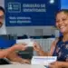 Atendente entregando nova Carteira de Identidade à cidadã, representando o mutirão de emissão de documento nos dias 26 e 27 de junho