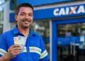 Trabalhador sorrindo segura cédulas de real em frente à Caixa, representando a liberação de até R$ 1.621 pela Caixa ou pelo Banco do Brasil.