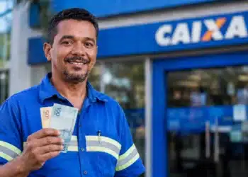 Trabalhador sorrindo segura cédulas de real em frente à Caixa, representando a liberação de até R$ 1.621 pela Caixa ou pelo Banco do Brasil.