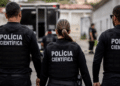 Agentes da Polícia Científica fardados de costas durante atuação em ocorrência.
