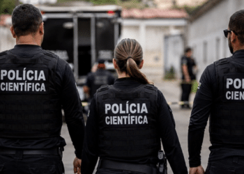 Agentes da Polícia Científica fardados de costas durante atuação em ocorrência.
