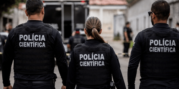 Agentes da Polícia Científica fardados de costas durante atuação em ocorrência.
