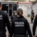 Agentes da Polícia Científica fardados de costas durante atuação em ocorrência.