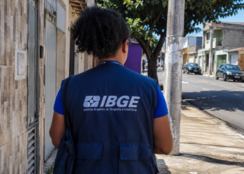 Profissional com uniforme do IBGE em rua residencial durante atividade de campo