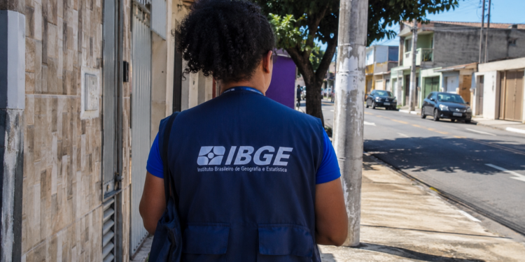 Profissional com uniforme do IBGE em rua residencial durante atividade de campo