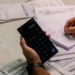 Pessoa calcula valores em celular enquanto organiza boletos e documentos de dívidas sobre a mesa.