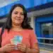Mulher segura cédulas de real em frente a uma agência bancária azul, representando a nova liberação do saque-aniversário do FGTS.