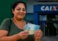 Mulher segura cédulas de reais em frente a uma agência da Caixa, representando o pagamento do Bolsa Família nesta terça-feira, dia 30 de junho.