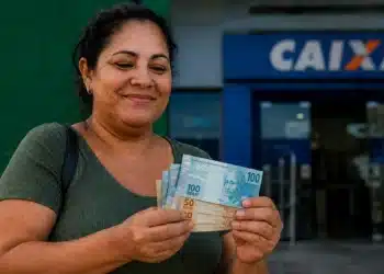 Mulher segura cédulas de reais em frente a uma agência da Caixa, representando o pagamento do Bolsa Família nesta terça-feira, dia 30 de junho.