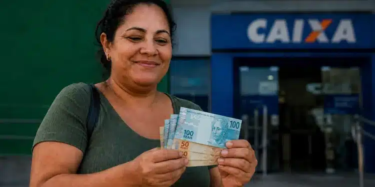 Mulher segura cédulas de reais em frente a uma agência da Caixa, representando o pagamento do Bolsa Família nesta terça-feira, dia 30 de junho.