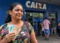 Mulher brasileira em frente a uma agência bancária da Caixa segurando dinheiro, representando o pagamento do Bolsa Família em junho.