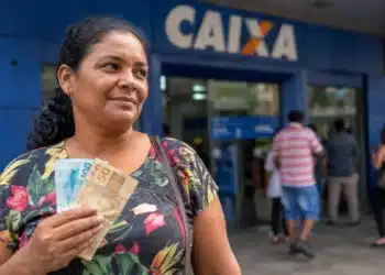 Mulher brasileira em frente a uma agência bancária da Caixa segurando dinheiro, representando o pagamento do Bolsa Família em junho.