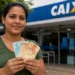 Mulher segura cédulas de real em frente a uma agência bancária da Caixa, representando o pagamento do Bolsa Família de junho de 2026.
