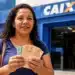 Mulher exibe cédulas de dinheiro em frente à agência da Caixa, representando a confirmação de pagamento de benefício no valor de R$ 6.220.
