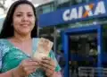 Mulher segura notas de reais em frente a uma agência da Caixa, em referência aos pagamentos de R$ 850, R$ 950 e R$ 1.050.