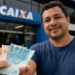 Homem recebe cédulas de real em frente a uma agência da Caixa, representando pagamento de R$ 1.000 que será liberado para CPFs com finais 0 a 9.