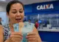 Mulher segura cédulas de real em agência da Caixa, representando o pagamento de R$ 2.900.