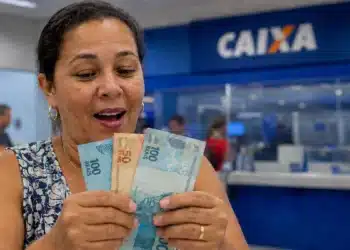 Mulher segura cédulas de real em agência da Caixa, representando o pagamento de R$ 2.900.