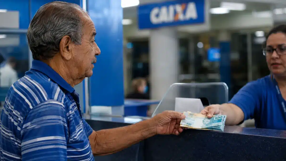 Idoso brasileiro recebendo cédulas de dinheiro em agência bancária, representando o pagamento do INSS nesta segunda-feira, 8 de junho.