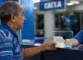Idoso brasileiro recebendo cédulas de dinheiro em agência bancária, representando o pagamento do INSS nesta segunda-feira, 8 de junho.