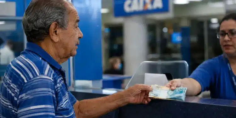 Idoso brasileiro recebendo cédulas de dinheiro em agência bancária, representando o pagamento do INSS nesta segunda-feira, 8 de junho.