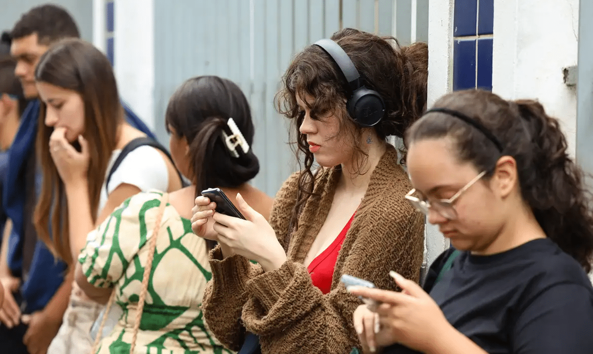 Estudantes consultam o celular do lado de fora do local de prova do Enem encostados na parede
