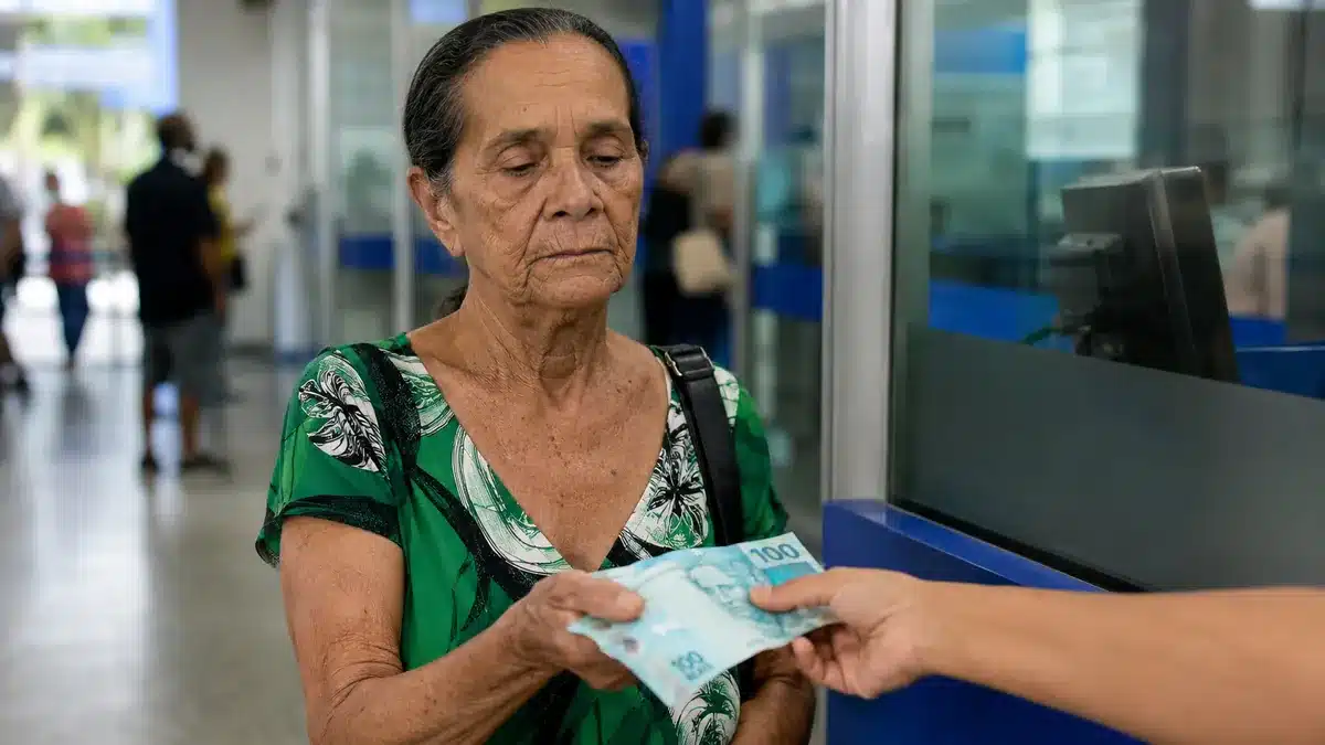 Mulher idosa recebendo pagamento do INSS em agência bancária brasileira