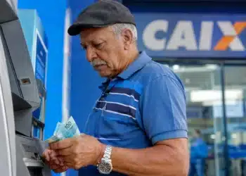 Beneficiário do INSS retira dinheiro em caixa eletrônico da Caixa, representando o pagamento desta sexta-feira, 26 de junho.