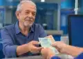 Idoso recebendo pagamento em agência do INSS, representando pagamentos no teto de R$ 8.475,55 liberados nesta semana.