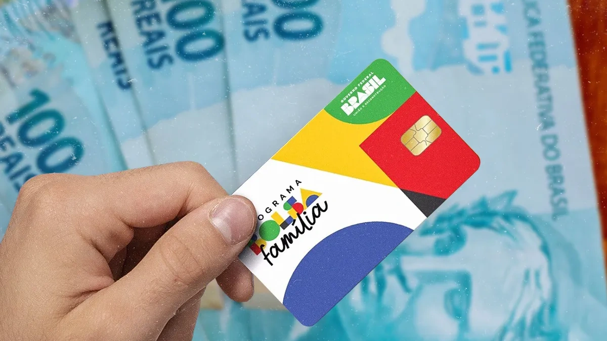 Mão segurando cartão do Bolsa Família sobre fundo com cédulas de real, representando o pagamento unificado do benefício em junho de 2026.