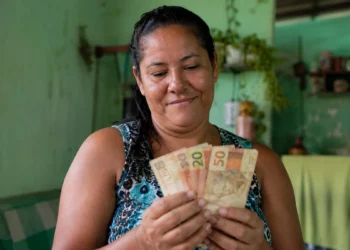 Mulher segurando cédulas de dinheiro em casa, em referência aos pagamentos de junho do Bolsa Família.