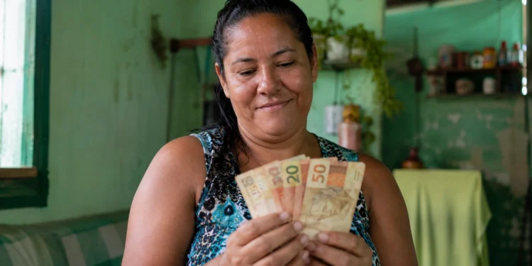 Mulher segurando cédulas de dinheiro em casa, em referência aos pagamentos de junho do Bolsa Família.