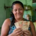 Mulher segurando cédulas de dinheiro em casa, em referência aos pagamentos de junho do Bolsa Família.