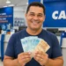Homem sorrindo em agência da Caixa, segurando cédulas de real, representando a liberação de pagamentos de até R$ 5.121 em junho de 2026.