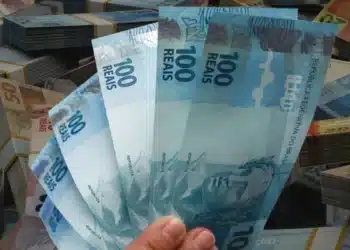 Mão segurando notas de 100 reais, representando pagamento de até R$ 1.625 do programa Pé-de-Meia, previsto para liberação na próxima semana.