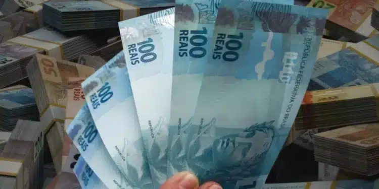 Mão segurando notas de 100 reais, representando pagamento de até R$ 1.625 do programa Pé-de-Meia, previsto para liberação na próxima semana.