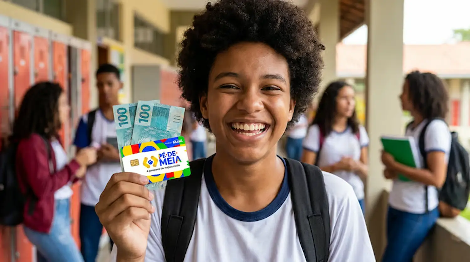 Aluno sorridente segura cartão do Pé-de-Meia e notas de dinheiro em corredor escolar.