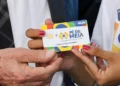 Mão segurando cartão do programa Pé-de-Meia durante liberação de pagamentos de R$ 1.000 no calendário de junho.