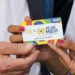 Mão segurando cartão do programa Pé-de-Meia durante liberação de pagamentos de R$ 1.000 no calendário de junho.