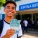 Estudante sorrindo em frente à escola segurando dinheiro, representando o pagamento do Pé-de-Meia de junho